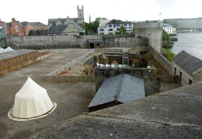 Courtyard with a large deep hole where the great hall was, a wooden rectangular building of the chapel and a small, white round campaign tent.