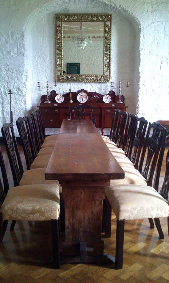 Long dining table with six chairs either side and one chair either end and a large large mirror overlooking the table at the far end of the room.