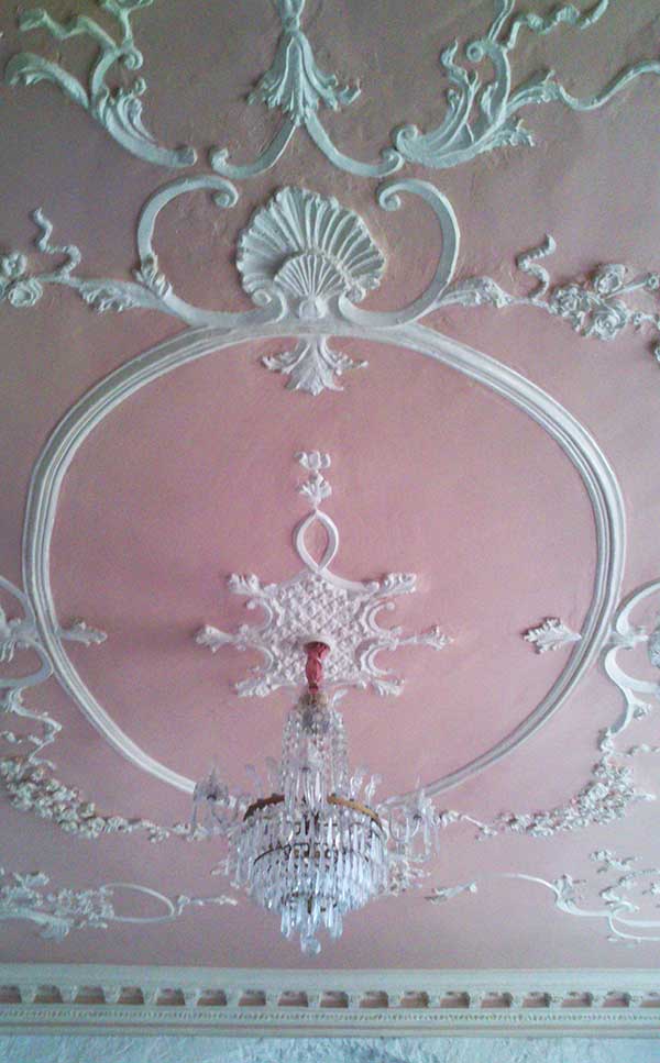 Another ornately ceiling, with white plasterwork, pink ceiling and a beautiful chandelier.