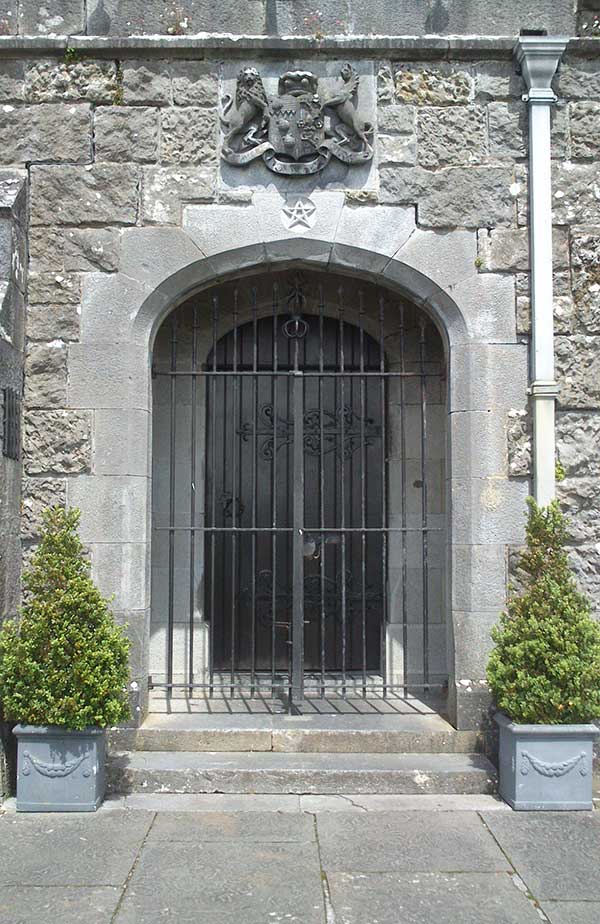 Round-topped wooden door behind closed bars, with stone crest above the doorway