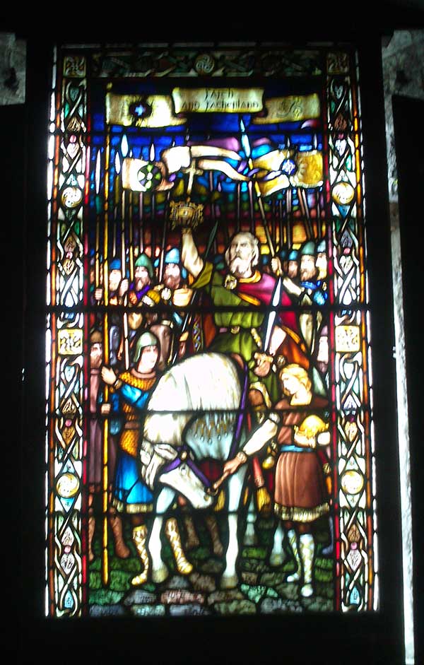 Stained glass window featuring a man on a horse (possibly a lord as he's holding what looks like a crown) surrounded by soldiers.